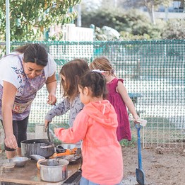 picture of teacher and three children in the mud kitchen outside 